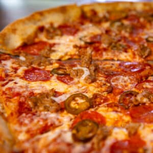 Close-up of a freshly baked pizza topped with melted cheese, pepperoni slices, sausage crumbles, and jalapeño peppers on a golden crust.