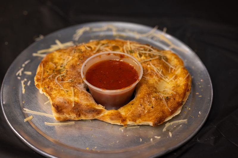A baked ring of folded pizza dough dusted with parmesan, with a cup of marinara in the middle
